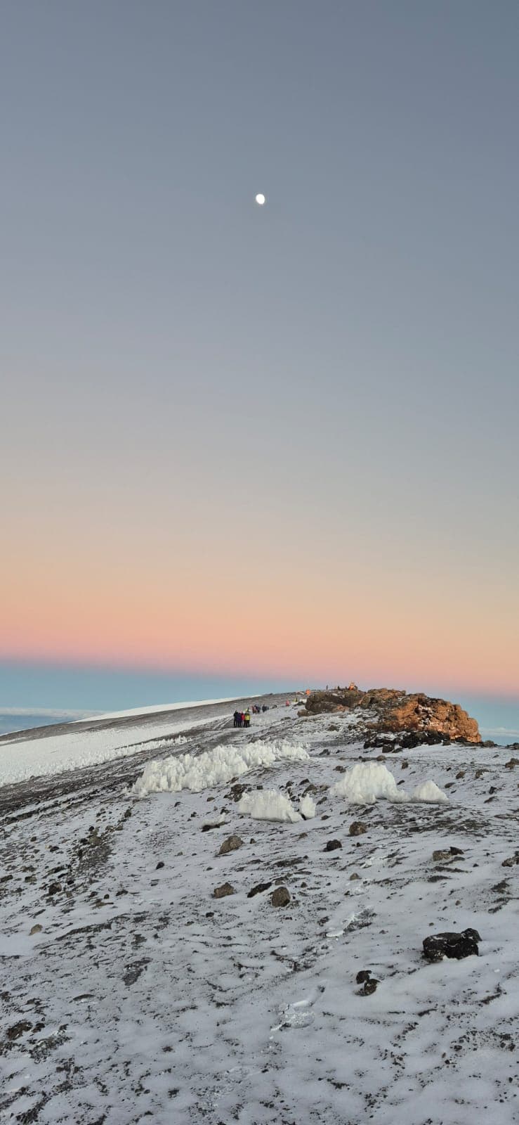 Kilimanjaro summit ridge at dawn with moon, climbers approaching the crater rim